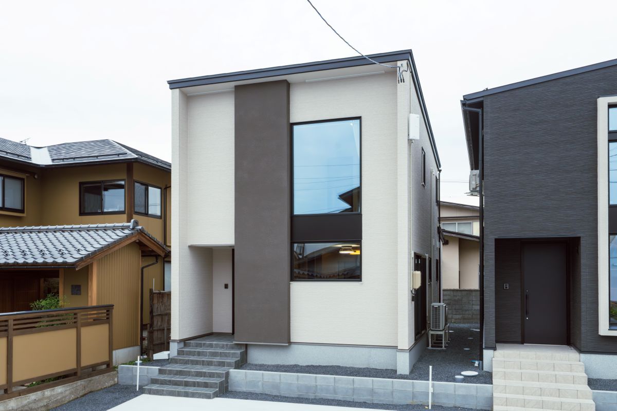 白い外壁に濃いグレーの縦ラインが特徴的な、シンプルモダンな二階建て住宅の外観。