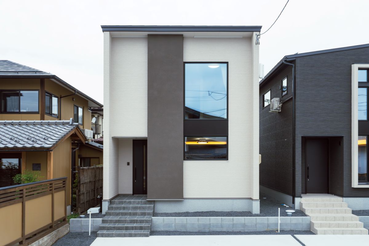 白い外壁にダークブラウンの縦ラインがアクセントのモダンな二階建て住宅。大きな縦長窓が特徴的なシンプルな外観。