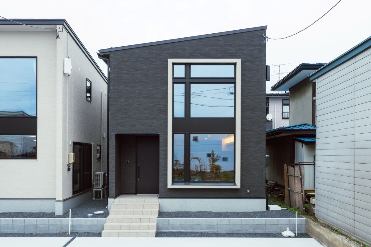 黒い外壁と片流れ屋根が特徴的なモダンな一戸建て住宅。白い窓枠の大きな縦長の窓がアクセントになっている外観。