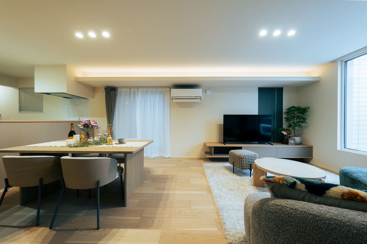 木製のテーブルとソファセットが置かれた、明るくモダンなリビングダイニングルーム。間接照明が空間を照らしている。