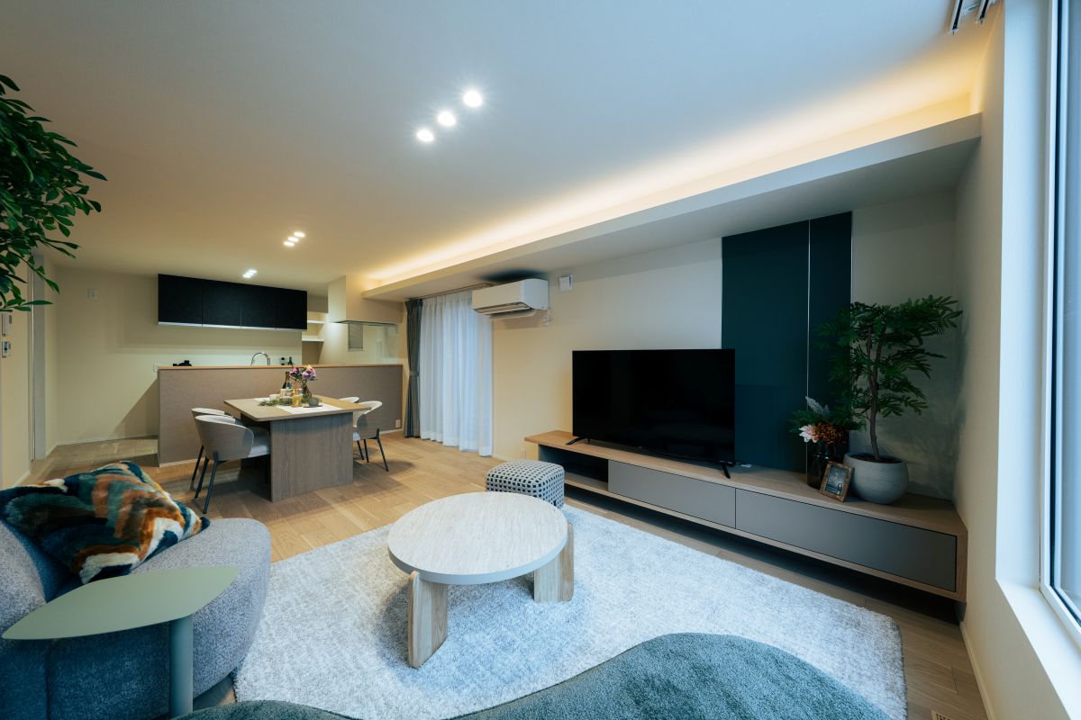 間接照明が照らすリビングダイニング。奥にダイニングスペース、手前にテレビボードが置かれ、ダークグリーンのアクセントクロスがおしゃれな内装。