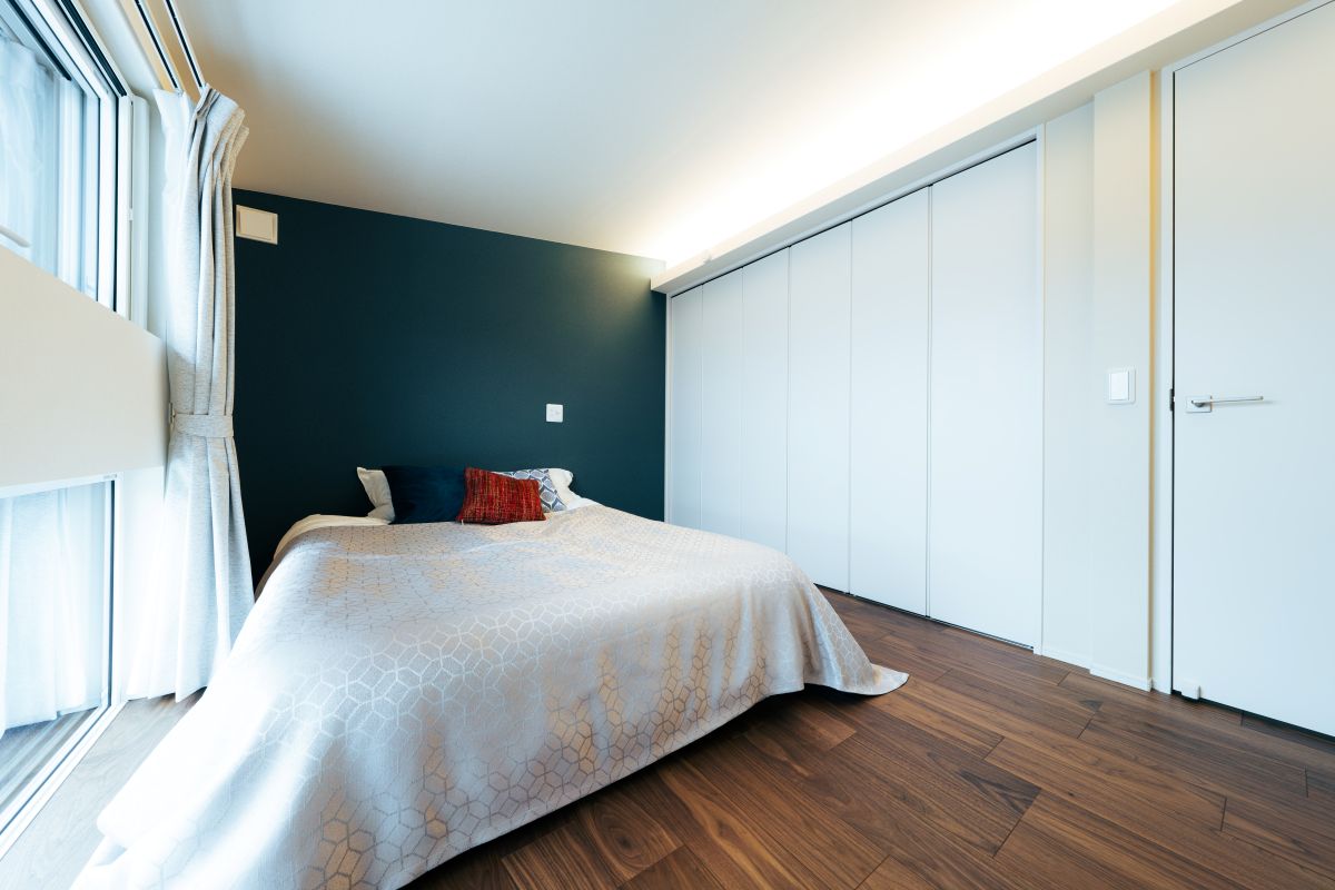落ち着いた雰囲気の寝室の内装。壁一面が濃いネイビーのアクセントクロスで、大きな白いクローゼットが設置されている。