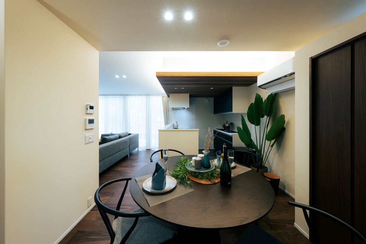 丸いダイニングテーブルからキッチンとリビングを望むLDK。木目調の天井と観葉植物がおしゃれな空間。