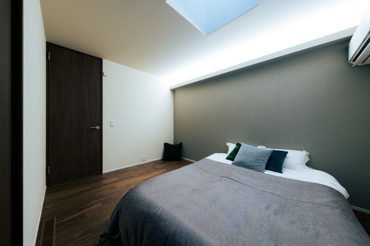 グレーのアクセントウォールと間接照明が落ち着いた雰囲気を演出する、天窓のあるモダンな寝室。