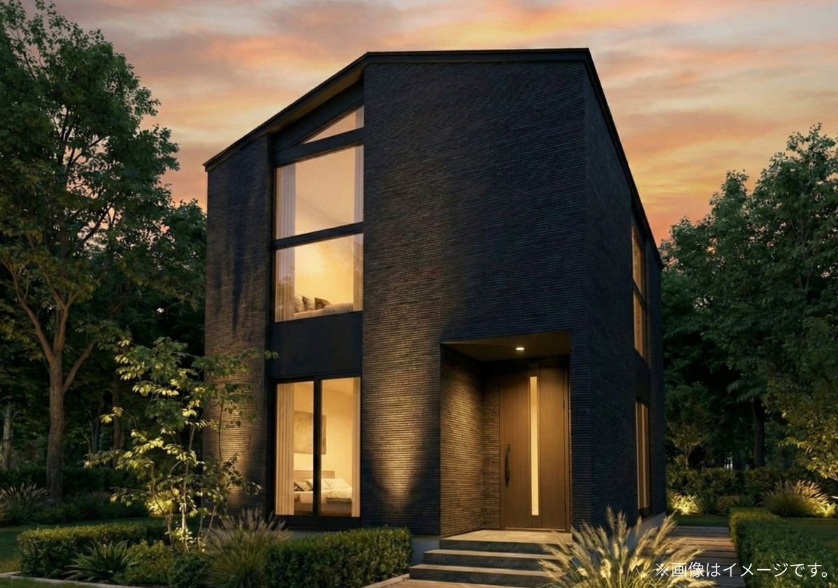 夕暮れに映えるモダンな黒い外壁の2階建て住宅。大きな窓からの暖かな光と植栽のライトアップが美しい、スタイリッシュな外観。