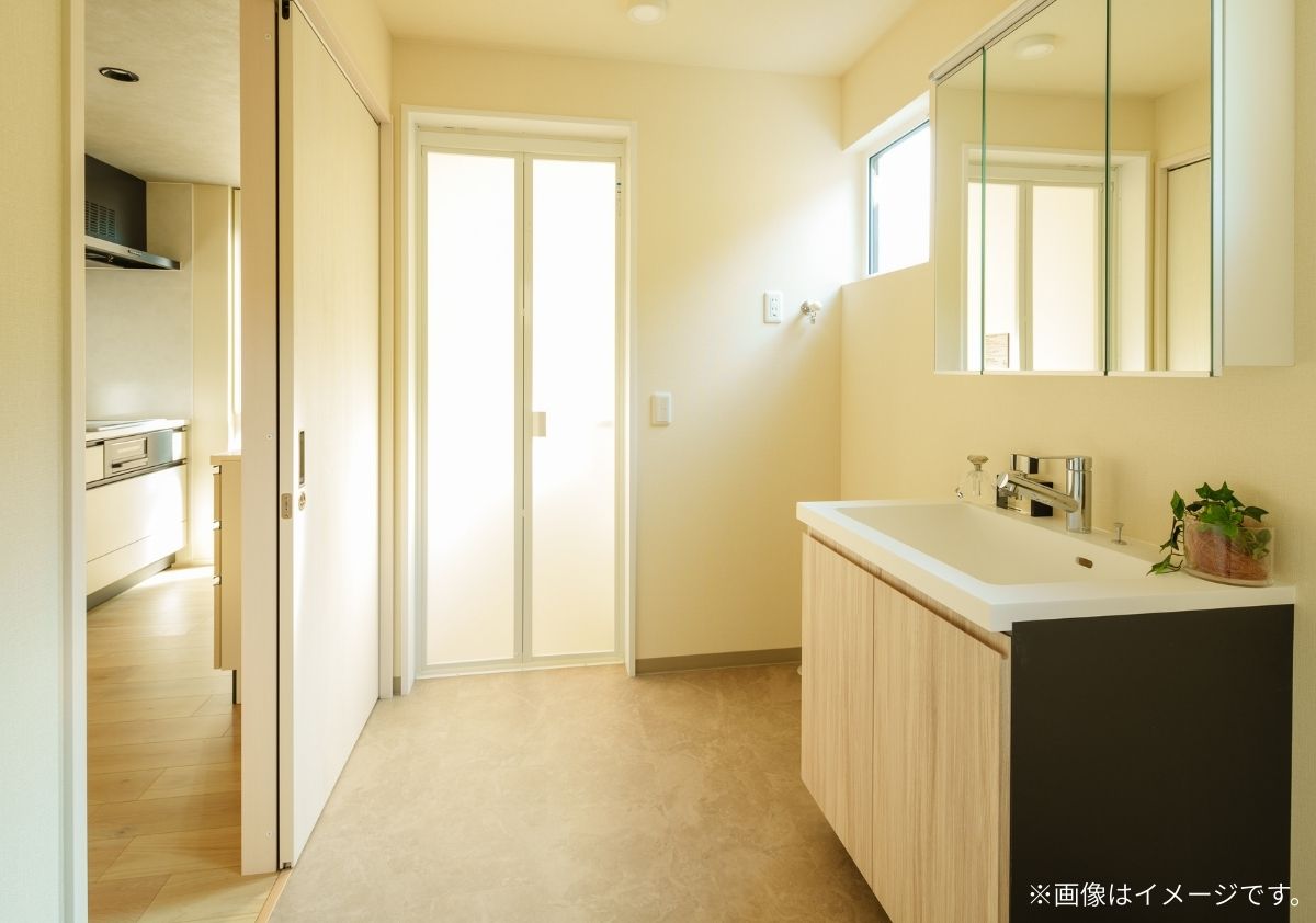 洗面脱衣室からキッチンへ直接移動できる、家事ラク動線を考慮した間取り。**明るい木目調の造作風洗面台と、自然光が差し込む高所窓が特徴の清潔感あふれる空間。