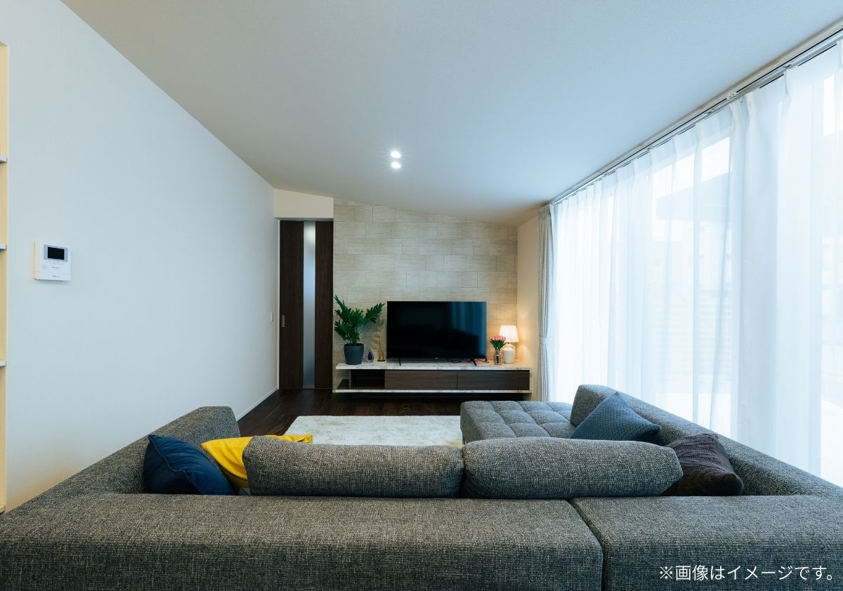 大きな掃き出し窓から光が差し込む明るいリビング。グレーのカウチソファと、テレビ背面の石目調アクセントウォールが調和したモダンなインテリア実例。