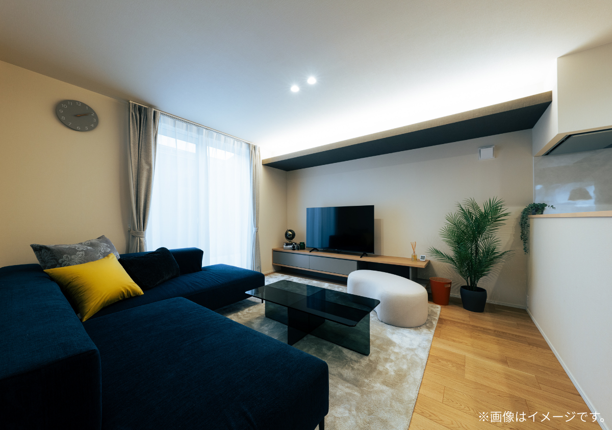 間接照明が温かみを添えるモダンなリビングルーム。 ネイビーのL字型ソファと木目調のフローリングが調和する、スタイリッシュな空間デザイン。