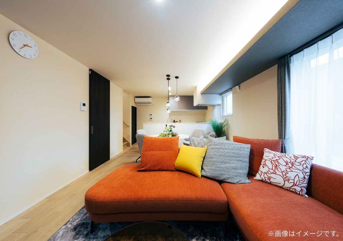 オレンジ色のL字型ソファが主役の縦長LDK。間接照明が美しい折り上げ天井と、黒のハイドアがアクセントのモダンなインテリア事例。